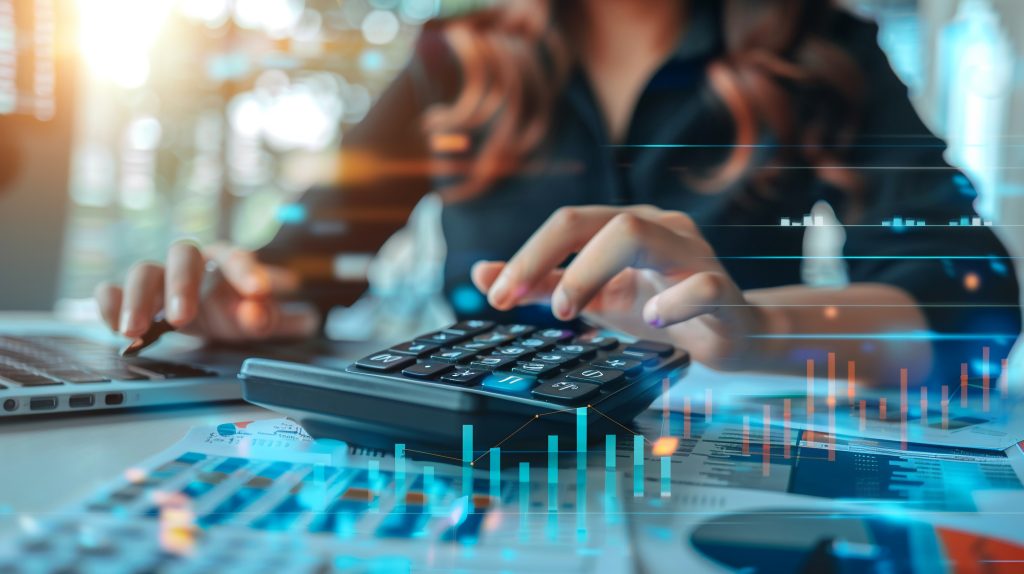 Auditoria fiscal e tributária: As mãos de uma pessoa usando uma calculadora em uma mesa com gráficos e tabelas financeiras holográficos.
