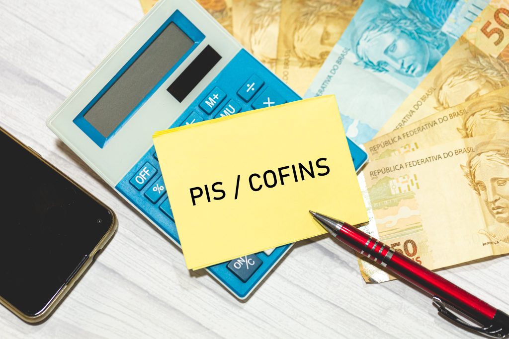 Um post-it amarelo com "PIS / COFINS" em uma mesa com calculadora, cartões de crédito e dinheiro. Itens relevantes para Créditos de PIS e COFINS para empresas de saúde.