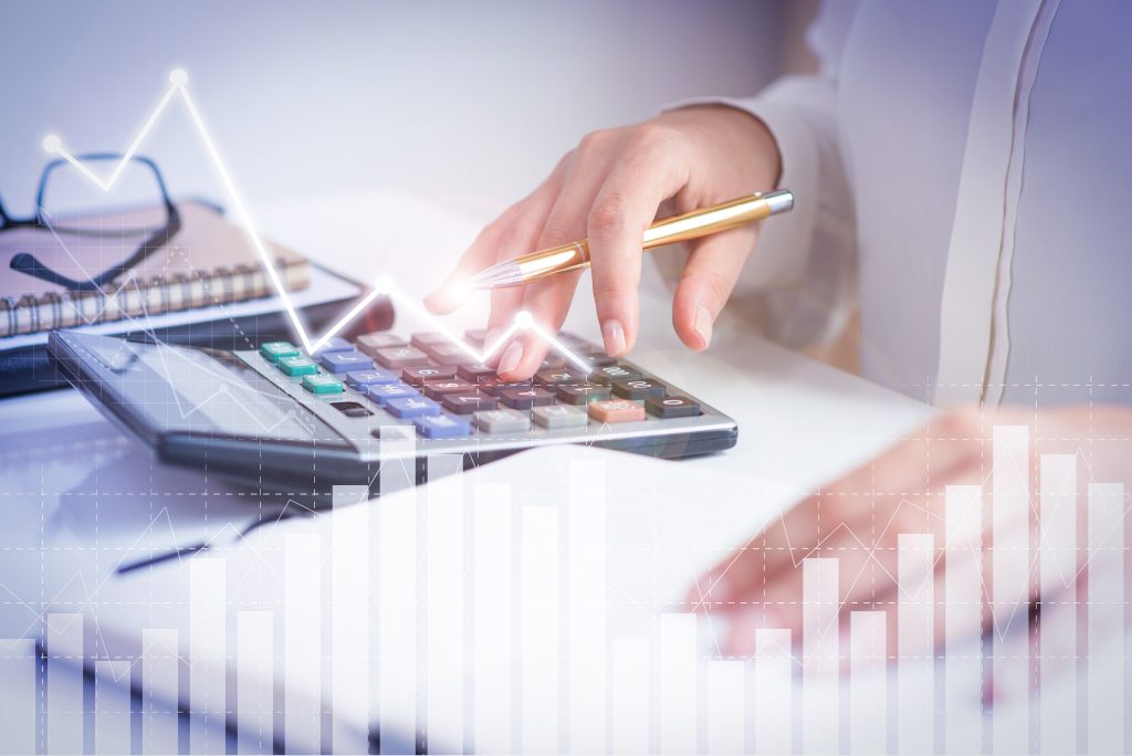 As mãos de uma pessoa usando uma calculadora e analisando dados financeiros com tabelas e gráficos holográficos. Esta tecnologia apoia o Planejamento tributário.