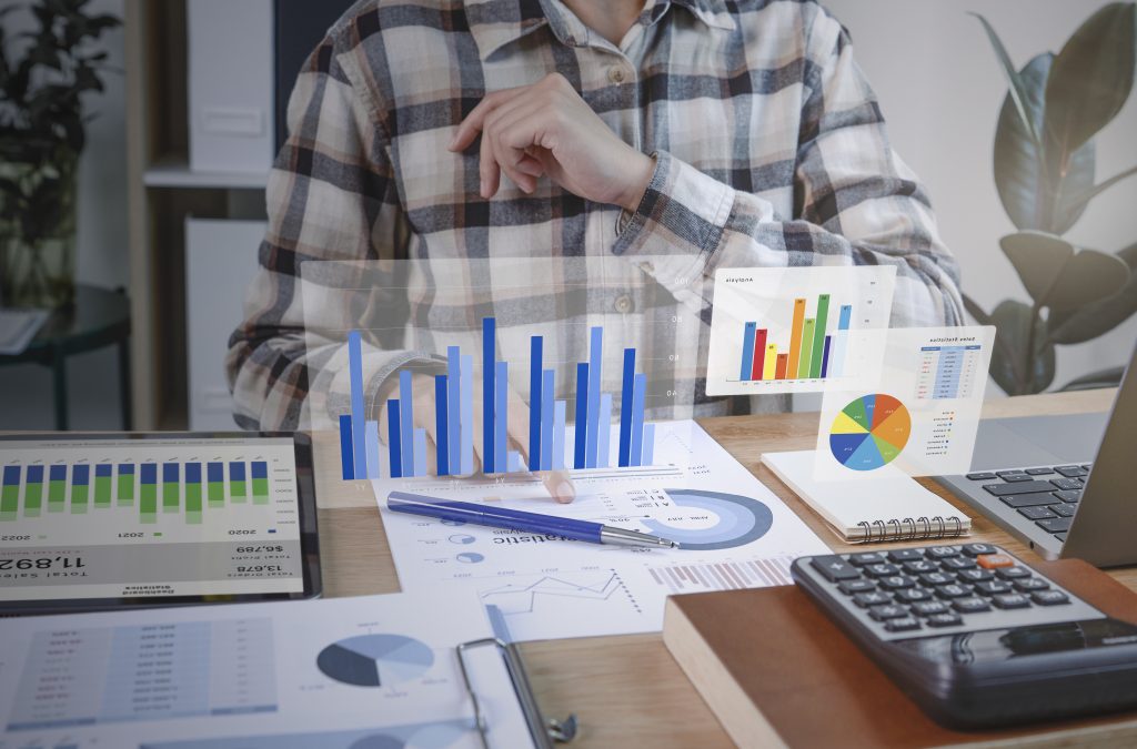 Um homem de meia-idade, vestindo uma camisa xadrez, analisa dados financeiros e gráficos em uma mesa com uma calculadora e outros materiais de escritório, tudo parte do Planejamento tributário.