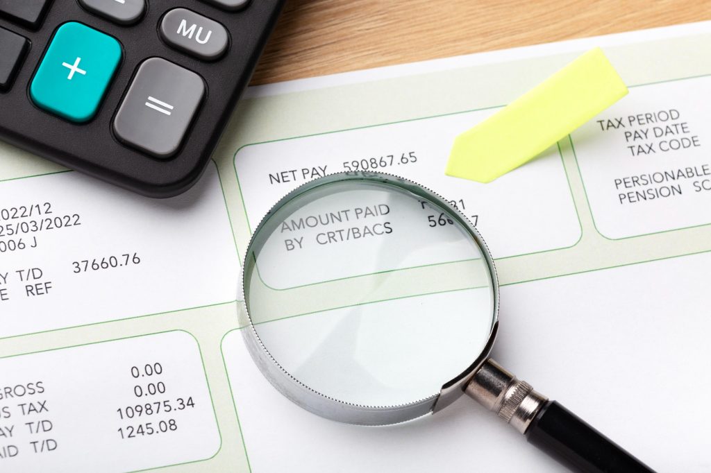 Lupa sobre documento financeiro com calculadora e marcador amarelo. Cena que ilustra a auditoria para garantir o Compliance fiscal.