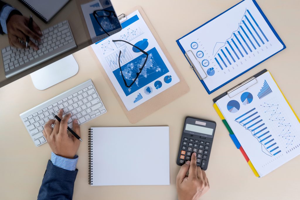 Mãos trabalhando em documentos financeiros, com gráficos e calculadora. Cena ilustra a aplicação de Estratégias de otimização tributária.