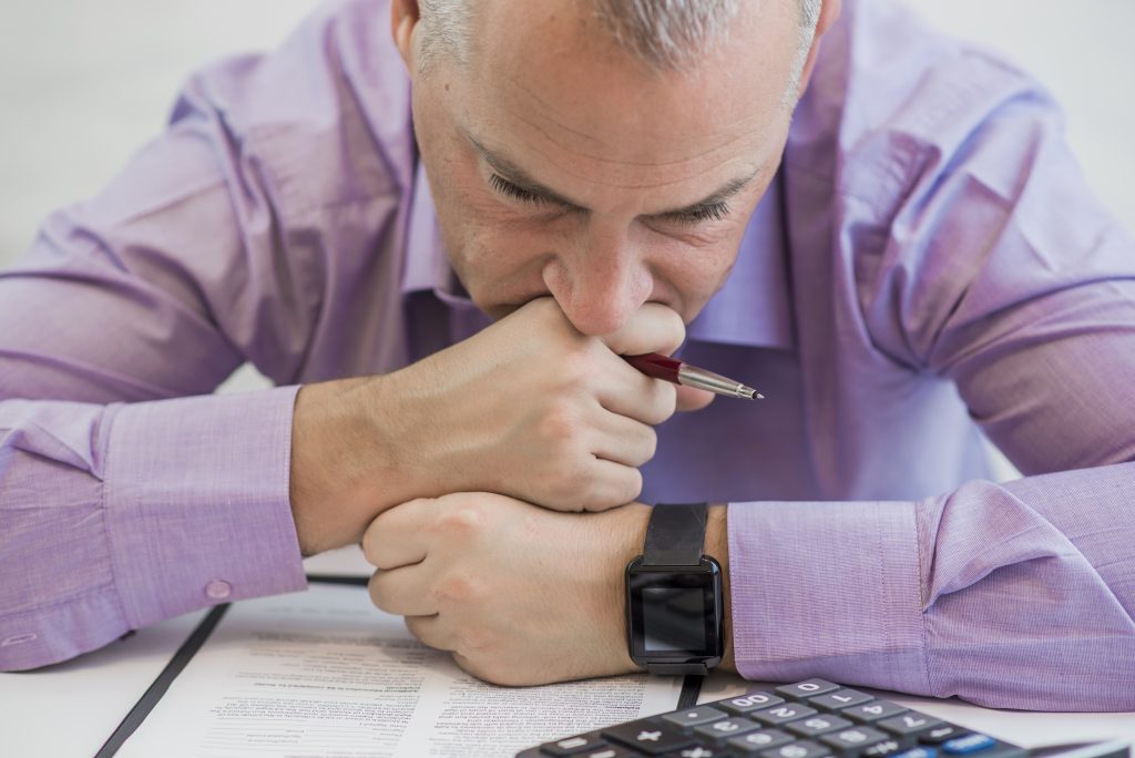 Homem concentrado em mesa cheia de documentos e calculadora. Sua expressão reflete o desafio de evitar o Pagamento Indevido de Taxas.