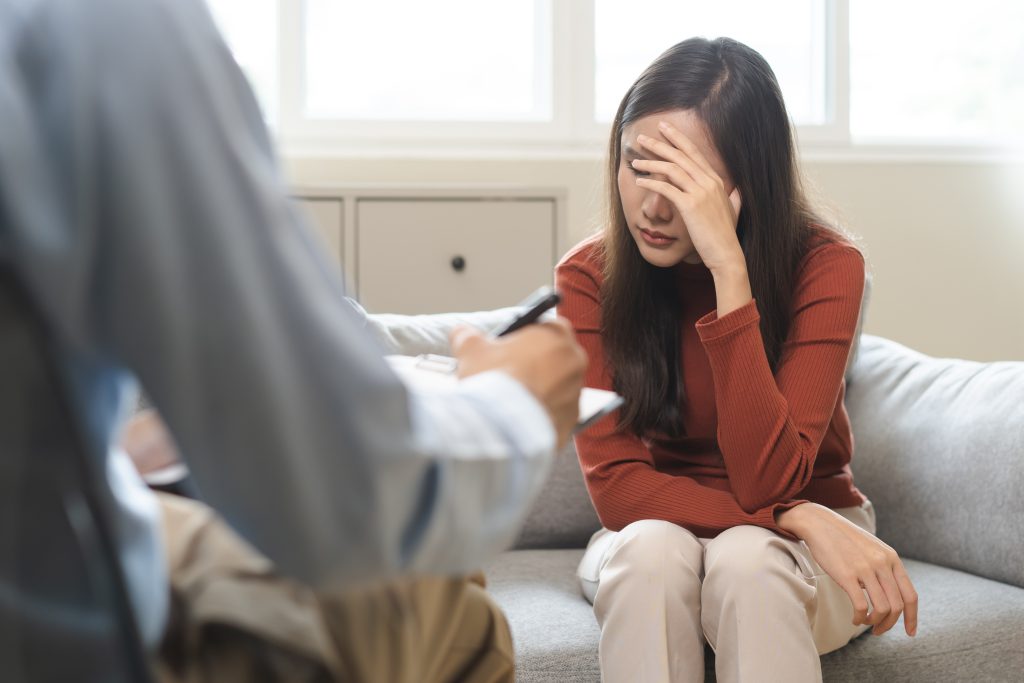 Mulher cabisbaixa em consulta enquanto profissional anota, representando um possível afastamento por saúde mental e a busca por apoio.