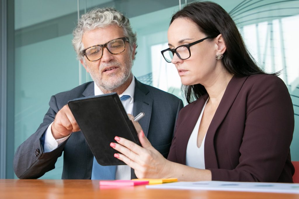 Dois executivos, um homem e uma mulher, em uma discussão séria, analisando dados em um tablet, possivelmente sobre como evitar a Insolvência empresarial.