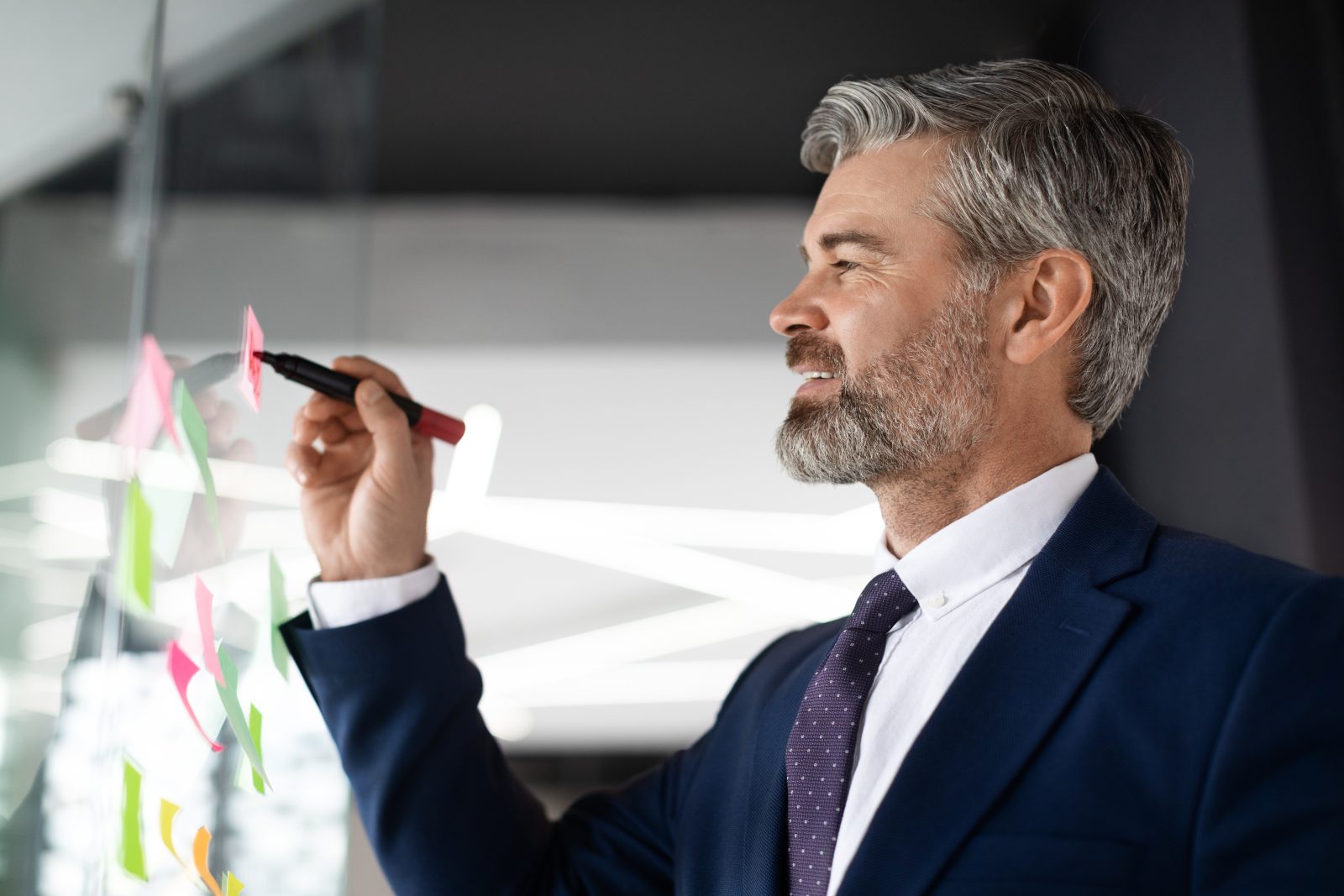 Executivo sênior organiza notas em vidro durante reunião de planejamento sucessório empresarial em escritório moderno.