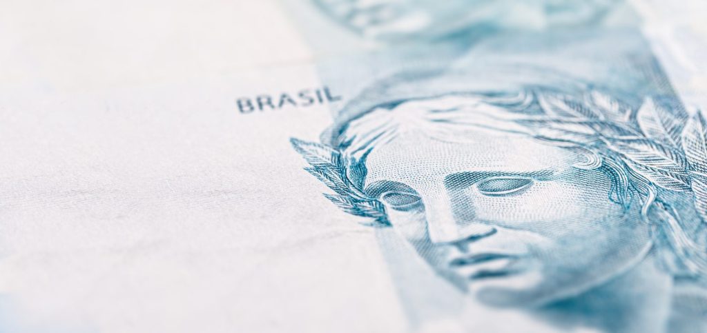 Detalhe de nota de cem reais brasileira, simbolizando a arrecadação e o peso do ICMS na economia.