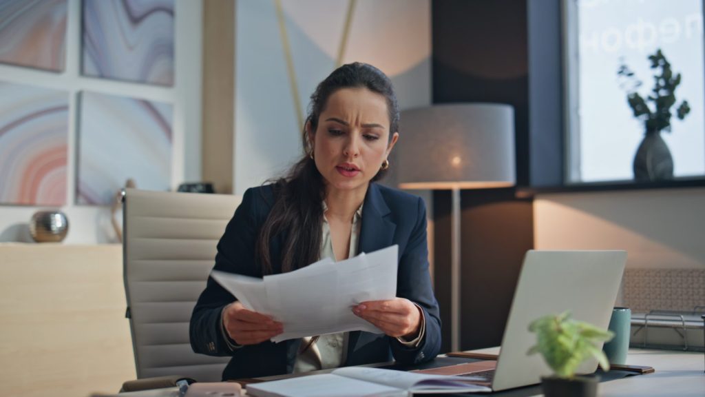 Empresária frustrada ao ler papéis de multas tributárias e autuações fiscais que prejudicam seu negócio.