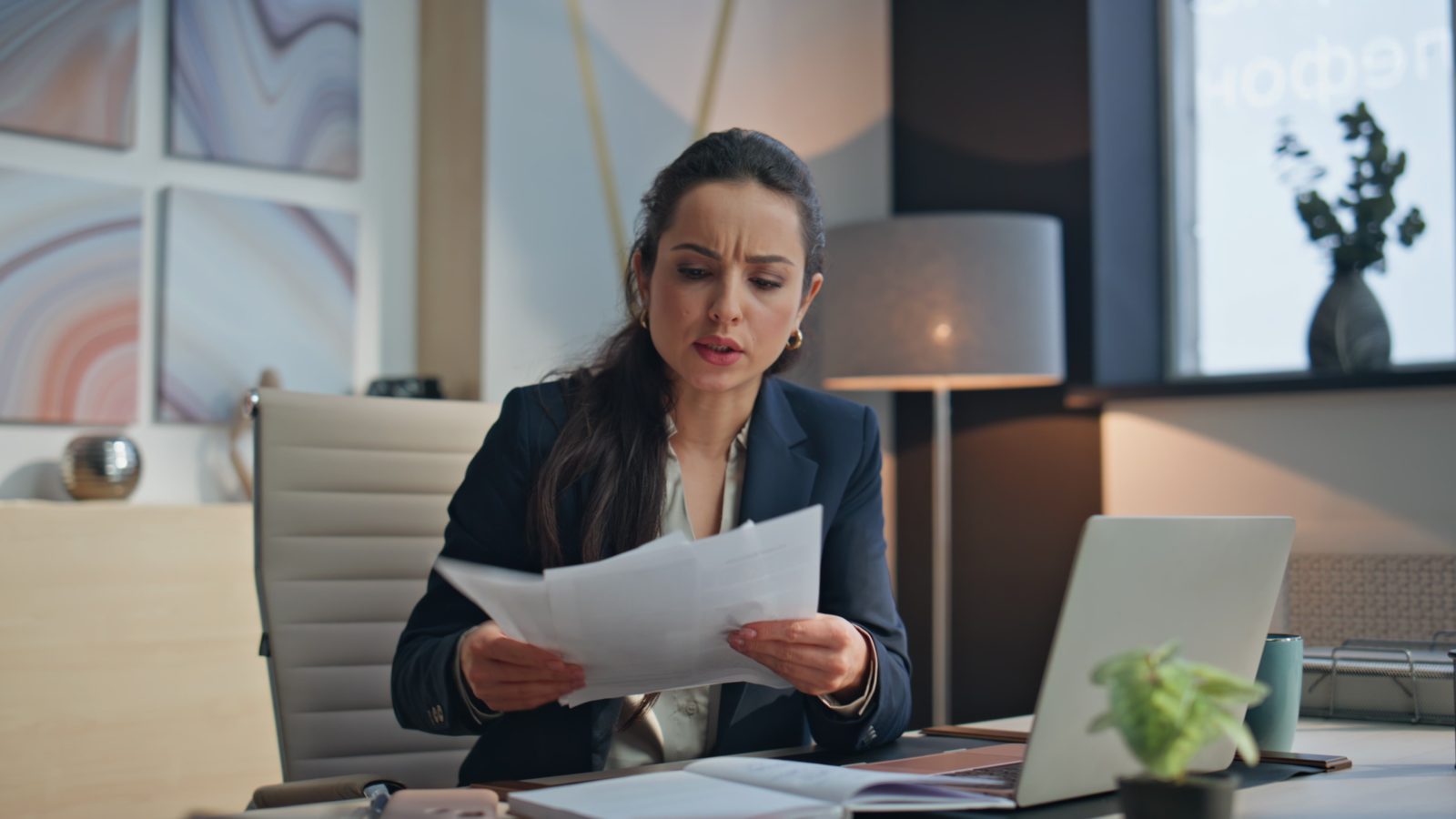 Empresária frustrada ao ler papéis de multas tributárias e autuações fiscais que prejudicam seu negócio.