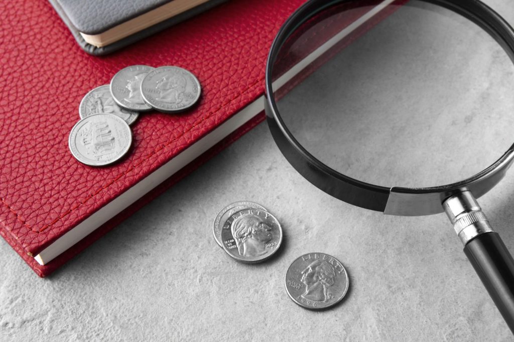 Lupa sobre papéis e moedas ao lado de um caderno, usada para avaliar os regimes tributários ideais para a empresa atual.