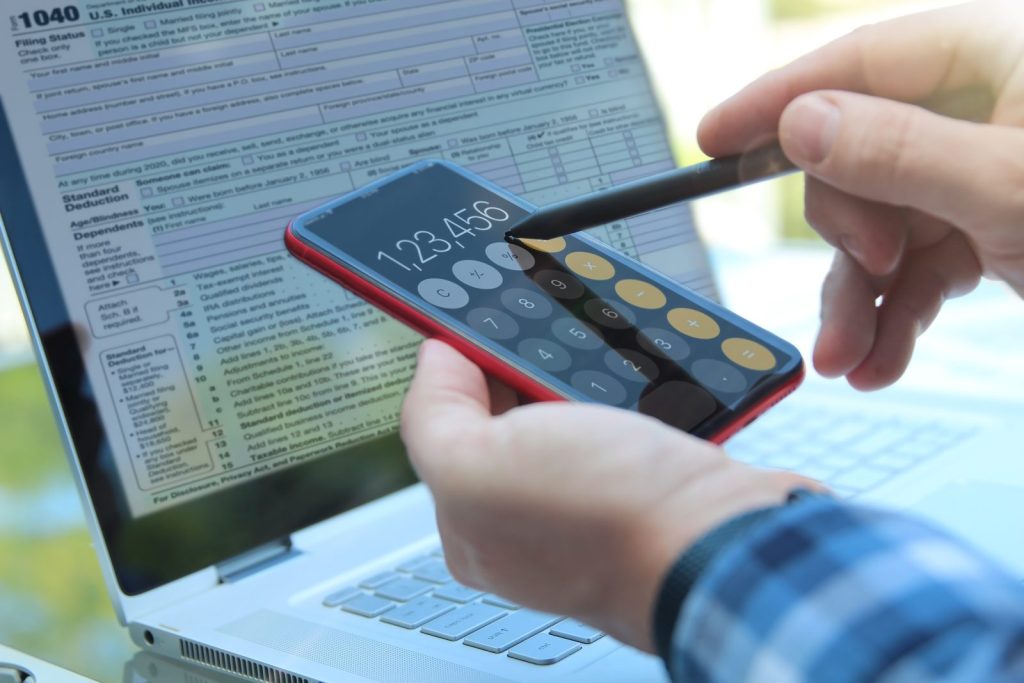 Profissional usando calculadora no celular durante revisão fiscal com formulário tributário ao fundo.