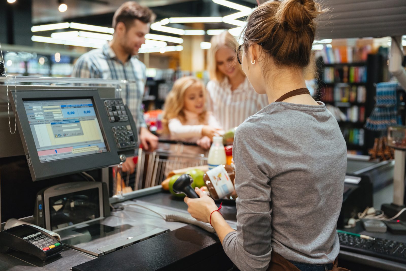 Caixa registrando compras de família em supermercado, cenário comum dos riscos jurídicos no varejo.