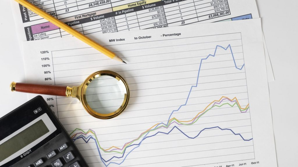 Gráficos financeiros em papel com calculadora, lápis amarelo e uma lupa dourada, que ilustram itens usados para mapear o crédito tributário.