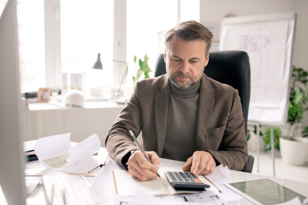 Empresário usando calculadora e anotando dados, representando o processo de regularização fiscal no varejo.
