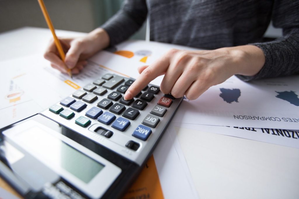 Mãos usando calculadora sobre relatórios financeiros durante processo de revisão tributária na empresa.
